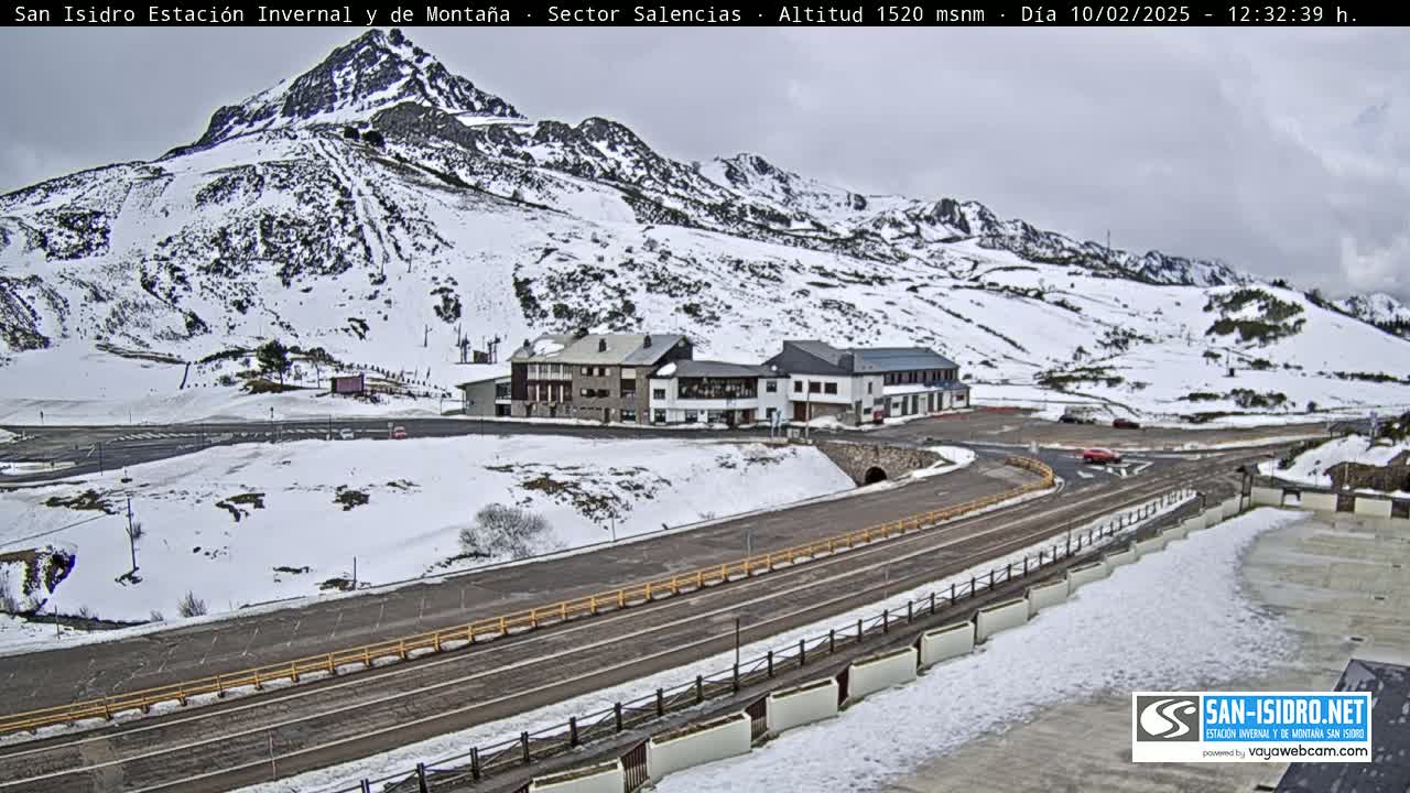 A snow-covered mountainside with a building complex and roads, under an overcast sky.