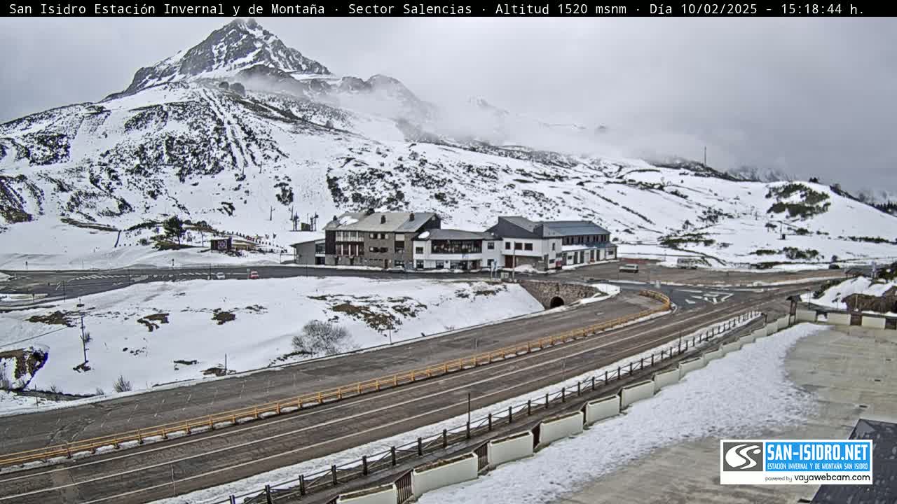 A snow-covered mountain landscape with a road and buildings, under an overcast sky.