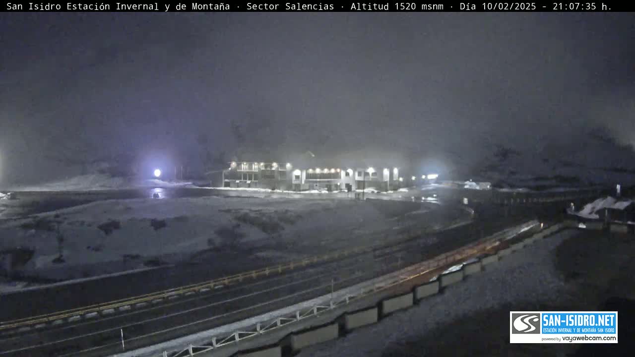 A snow-covered parking lot and roadway in front of a lit building are visible under a hazy, dark night sky.