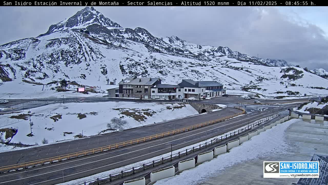 A snow-covered mountainside with a few buildings and roads is visible under an overcast sky.