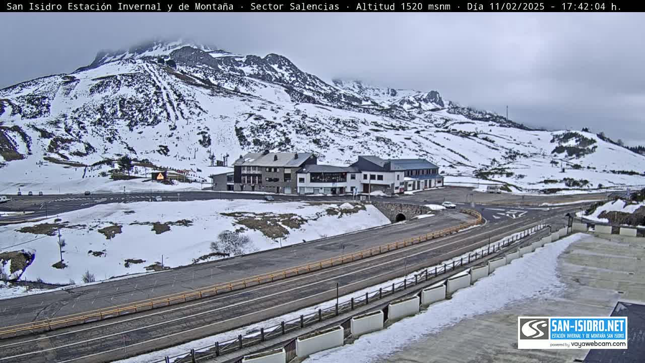 A snow-covered mountainside with a road and buildings at its base under an overcast sky.