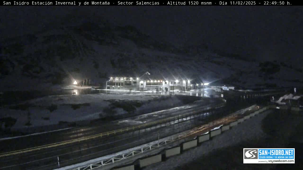 A brightly lit building sits near a dark, snow-covered mountain road at night.