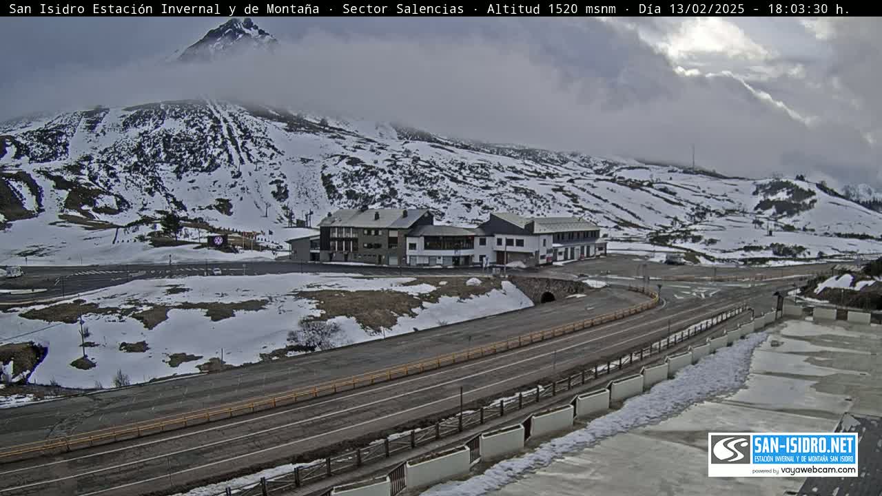 A snow-covered mountainside with a building complex and roads, under a cloudy sky.
