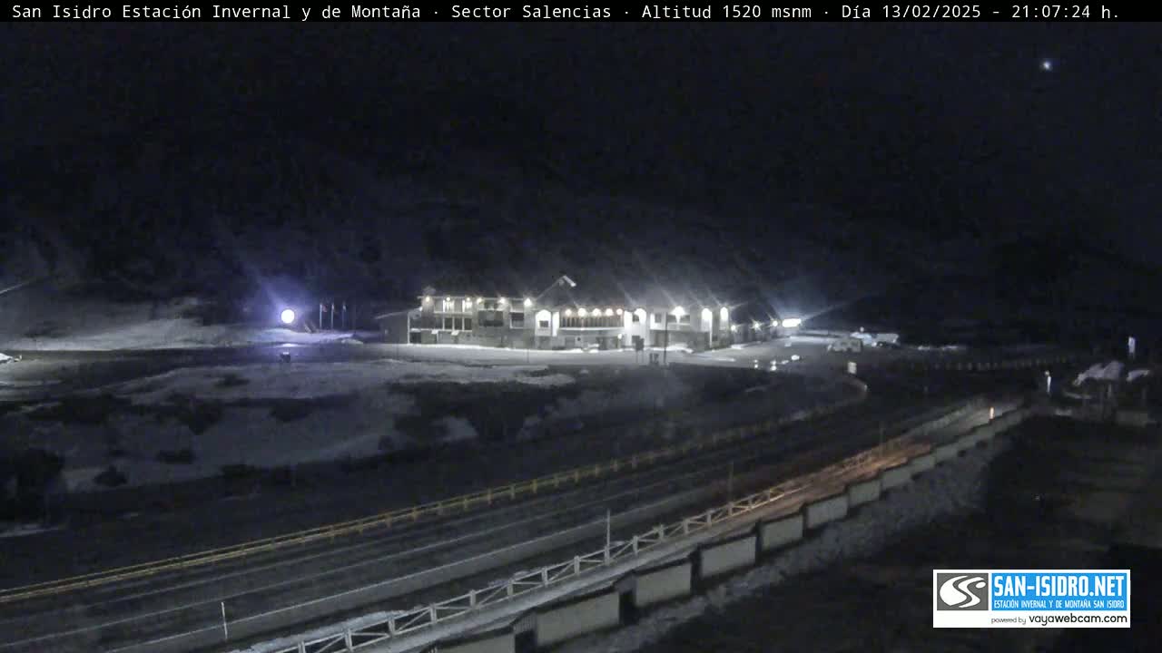 A large building is illuminated at night in a snow-covered area, with a road and guardrail visible below.