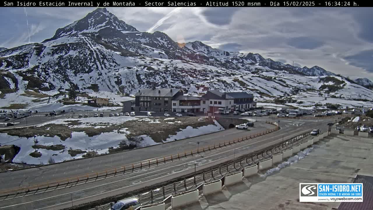 A mountain resort with snow-covered slopes and a parking lot is visible under partly cloudy skies.