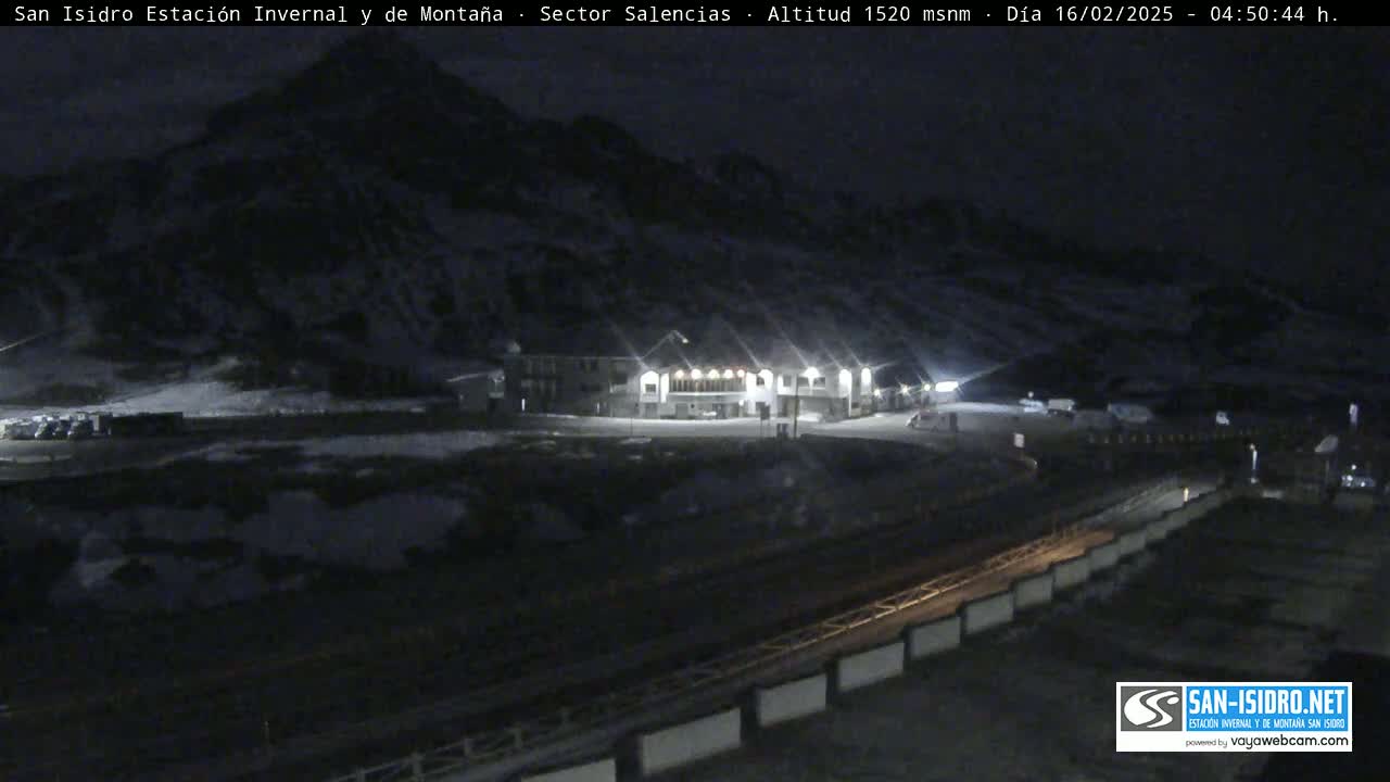A nighttime view of a snow-covered mountainside with a brightly lit building and a road in the foreground.