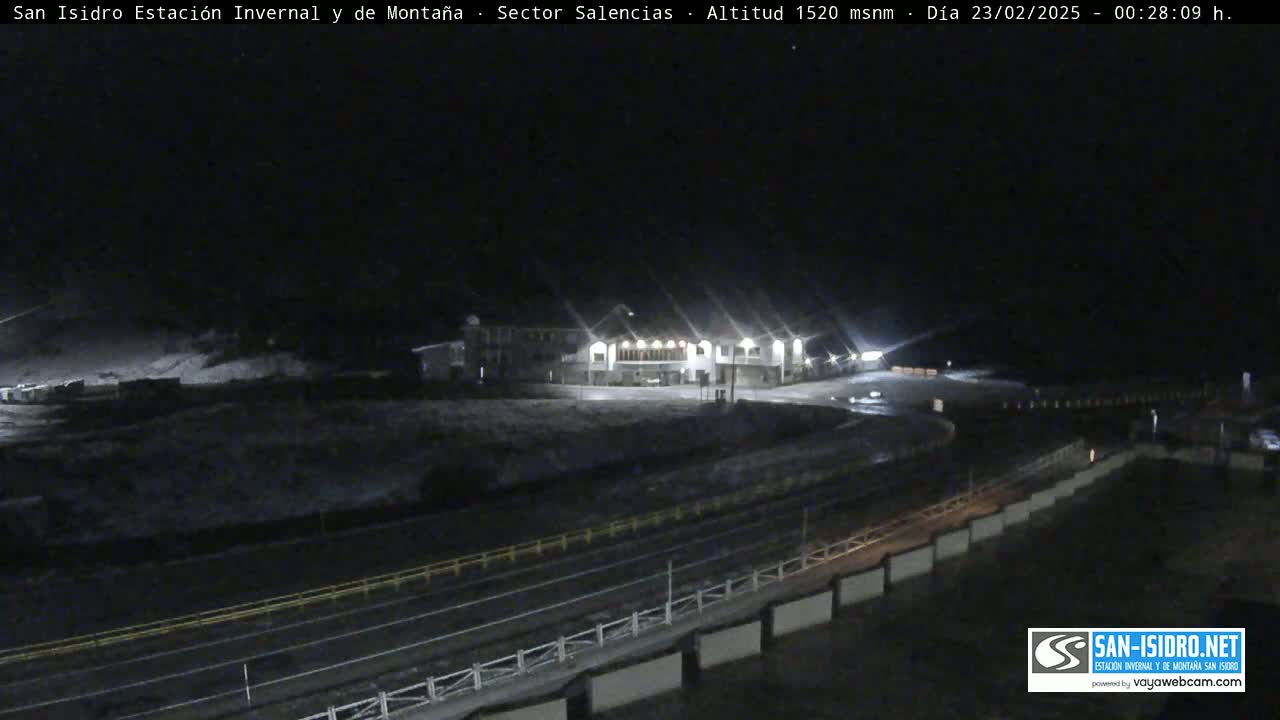 A nighttime view of a snow-covered mountain resort area with a lit building and roads.
