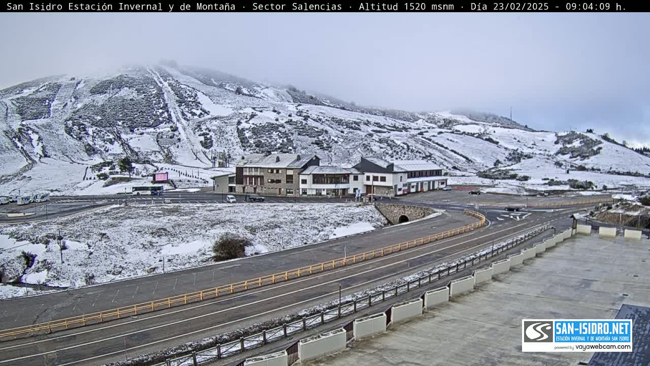 A snow-covered mountainside with a building complex and roads below, under an overcast sky.