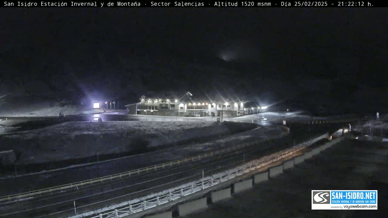 A nighttime view of a snow-covered mountain resort with a large building and roads illuminated by artificial light.