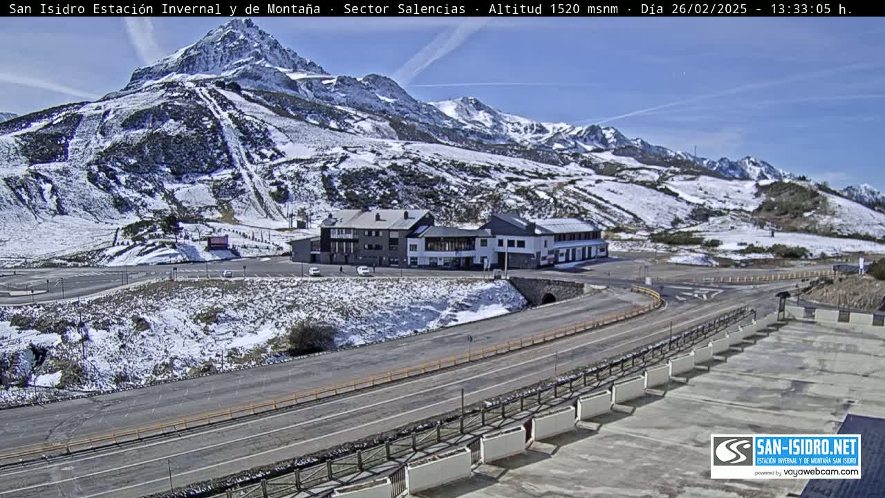 A mountain resort with snow-covered slopes and buildings is seen on a sunny day.