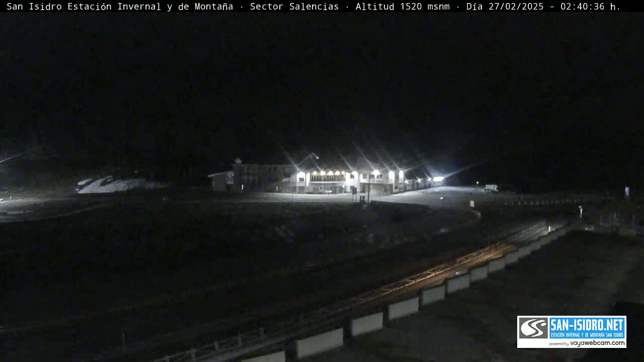 A brightly lit building sits in a snow-covered area at night.