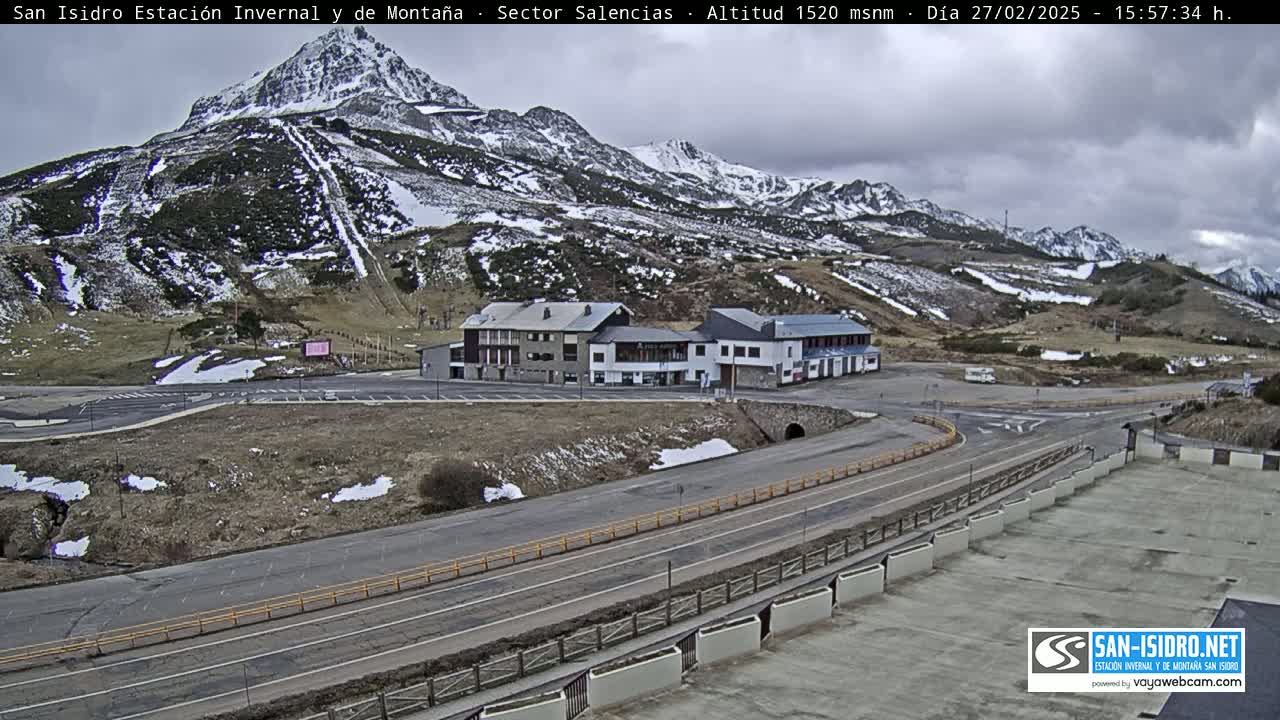 A mountainside with patchy snow, a roadway, and several buildings is visible under an overcast sky.
