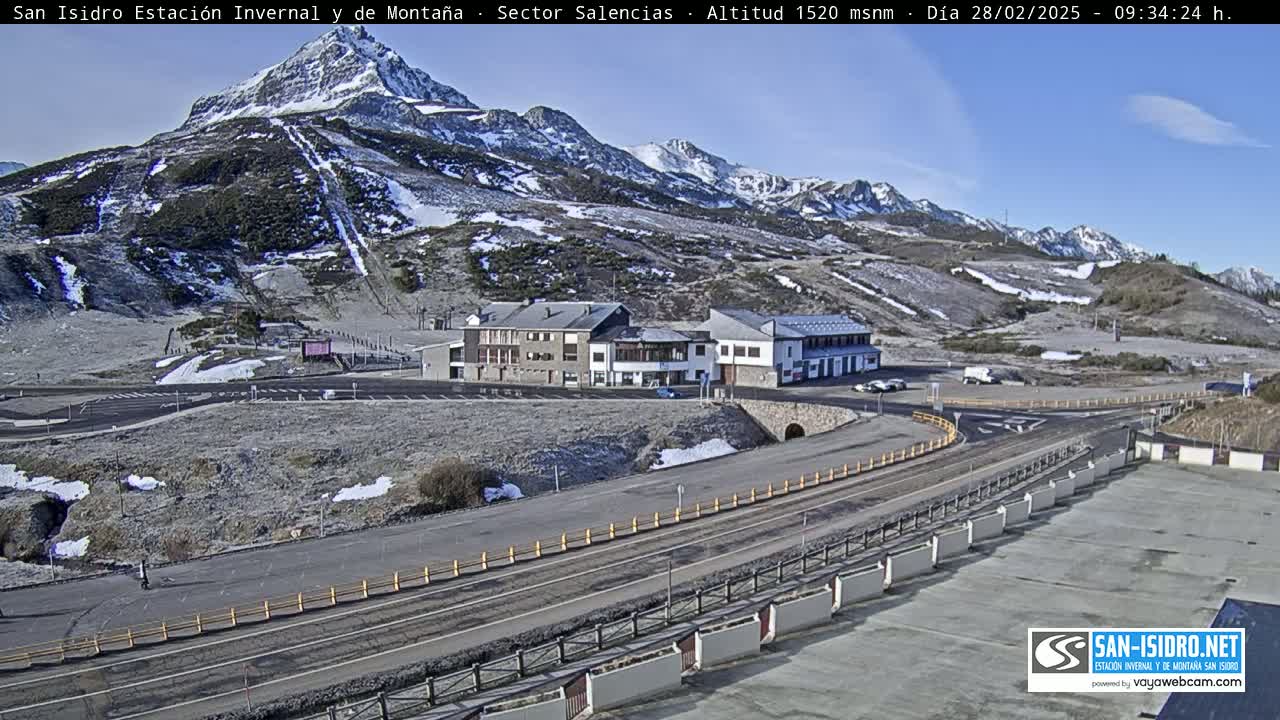 A mountain resort with snow-covered slopes and buildings is visible on a sunny day.