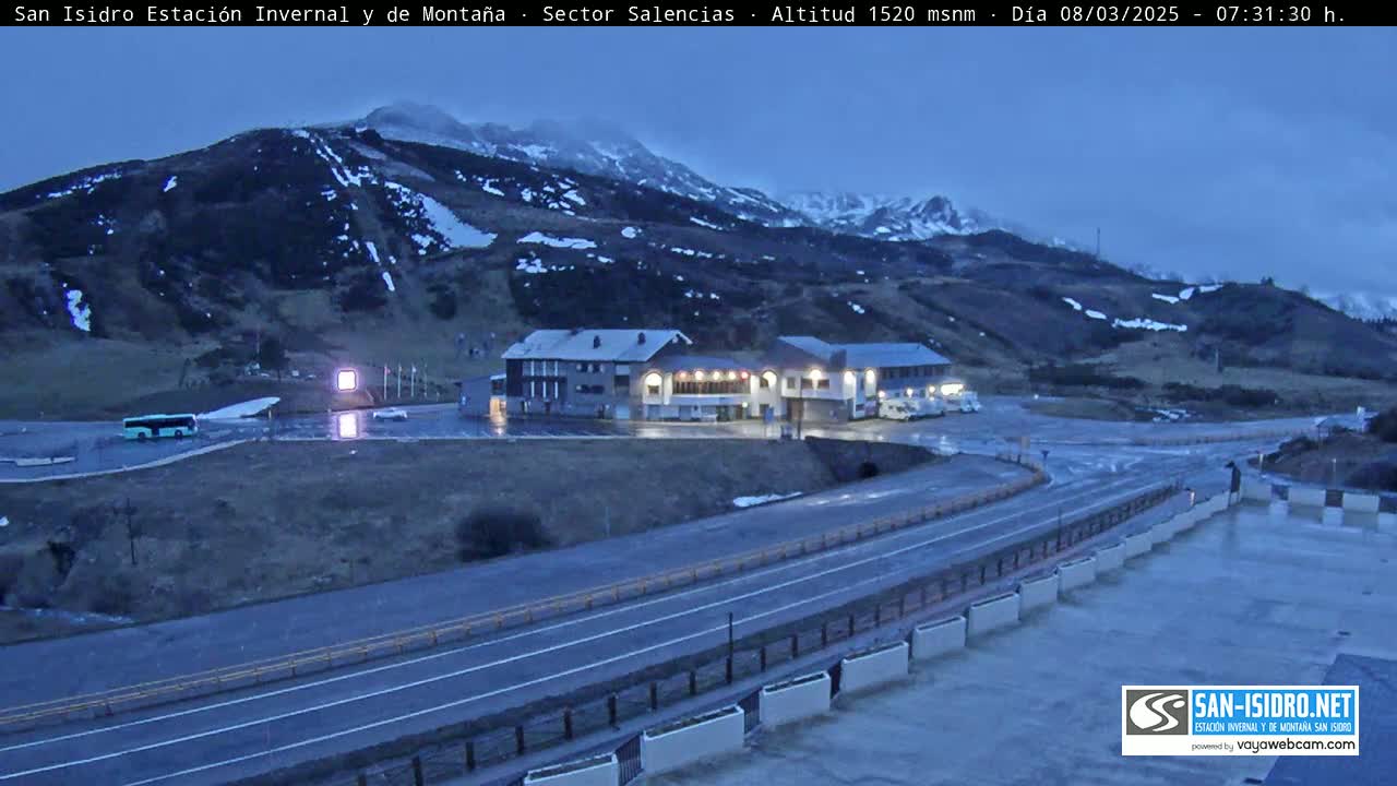 A mountainside resort area with two buildings and a road, under a twilight sky.