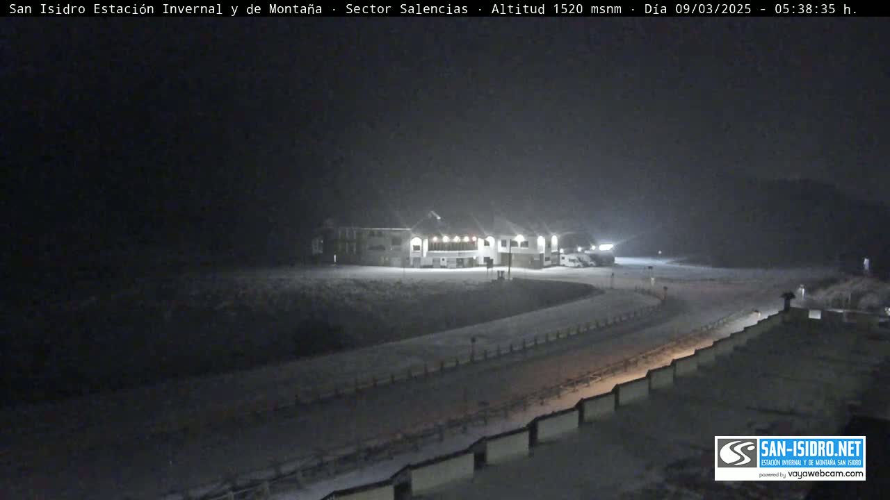A snow-covered road curves past a lit building at night.