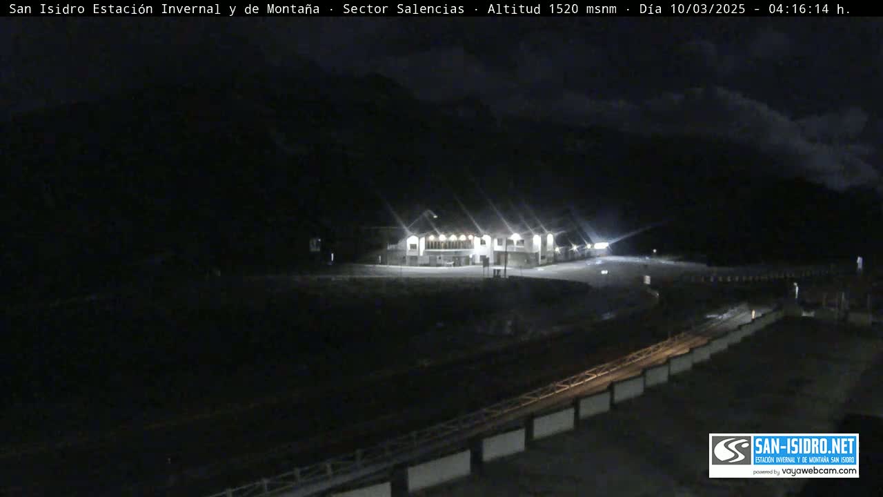A brightly lit building sits in a dark, mountainous area at night under a cloudy sky.