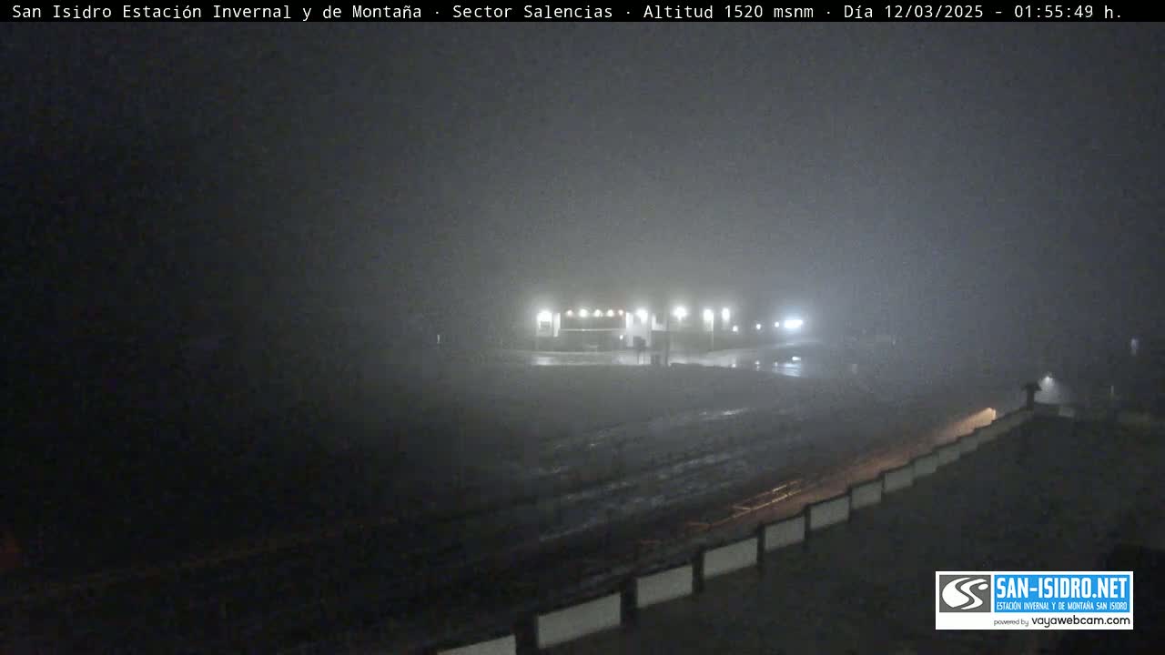 A foggy nighttime scene shows a building with lights on, and a road leading to it, all under a heavy fog.