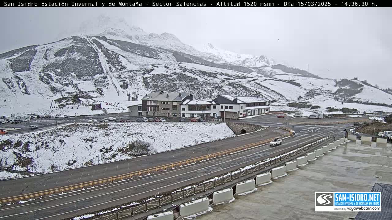 A snow-covered mountainside with ski slopes, a building complex, and roads, under an overcast sky.