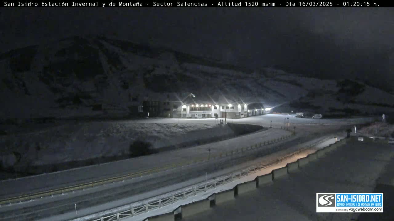 A snow-covered mountainside at night, illuminated by lights from a building near a road.