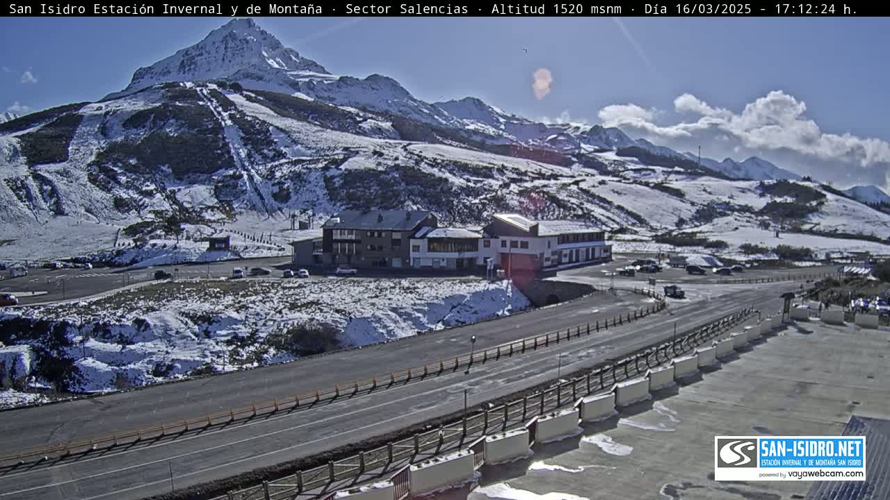A sunny day shows a snow-covered mountain with ski slopes and a building complex near a road.