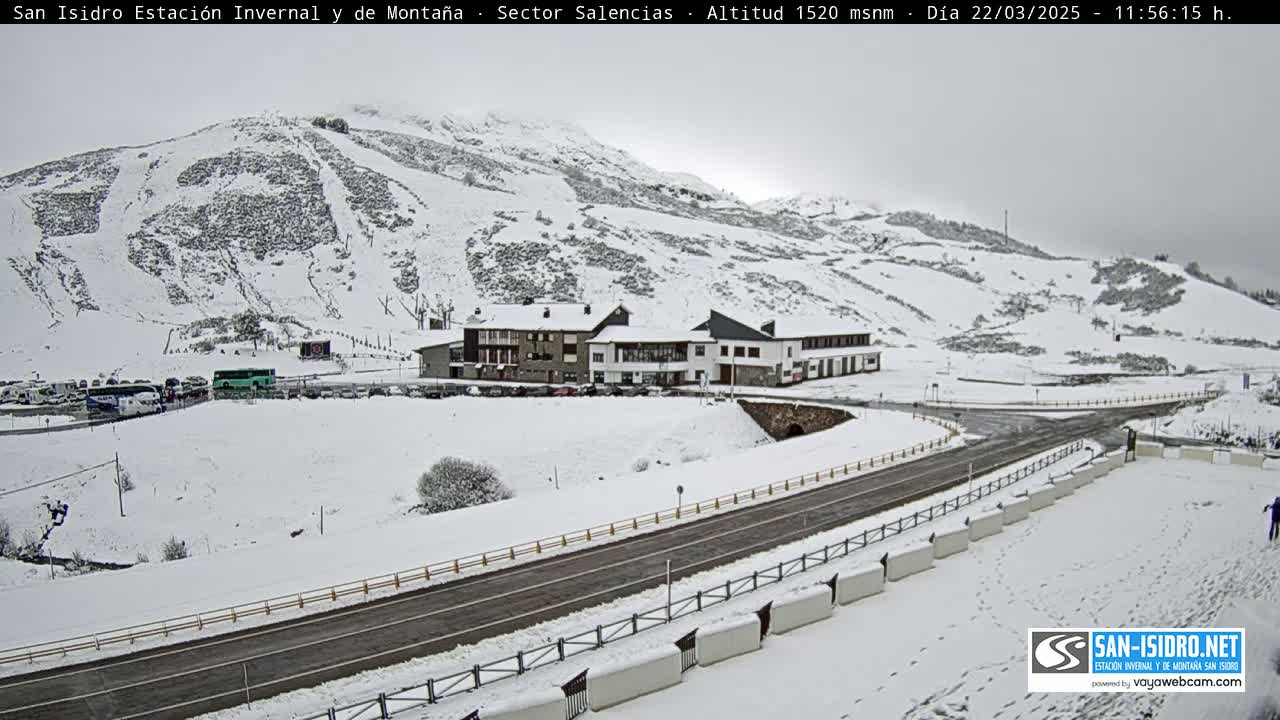 A snow-covered mountainside with a building and road, under an overcast sky.