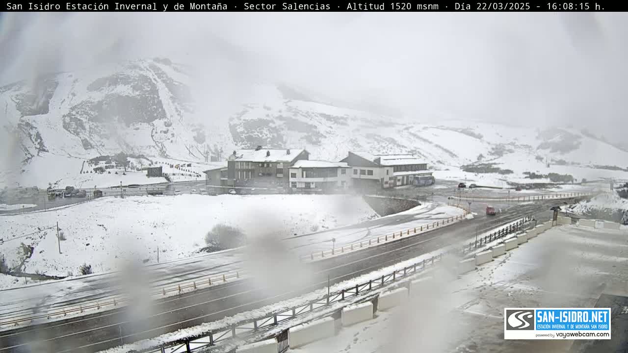 A snow-covered mountain landscape with a road and buildings, under hazy, snowy conditions.