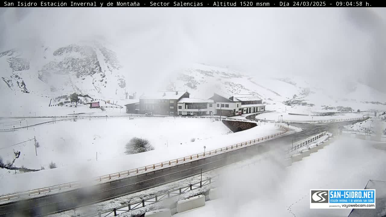 A snow-covered mountain resort with a building complex and roads is visible in hazy weather conditions.