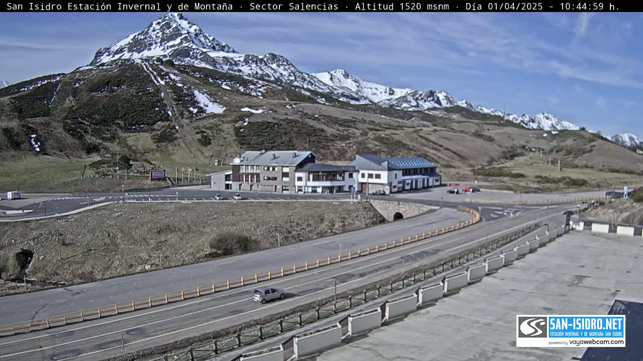 A sunny day reveals a mountain resort with buildings near a roadway, nestled below snow-capped mountains.