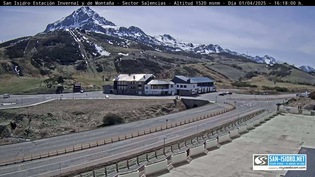 A mountain resort area with a parking lot and buildings under a mostly sunny sky.