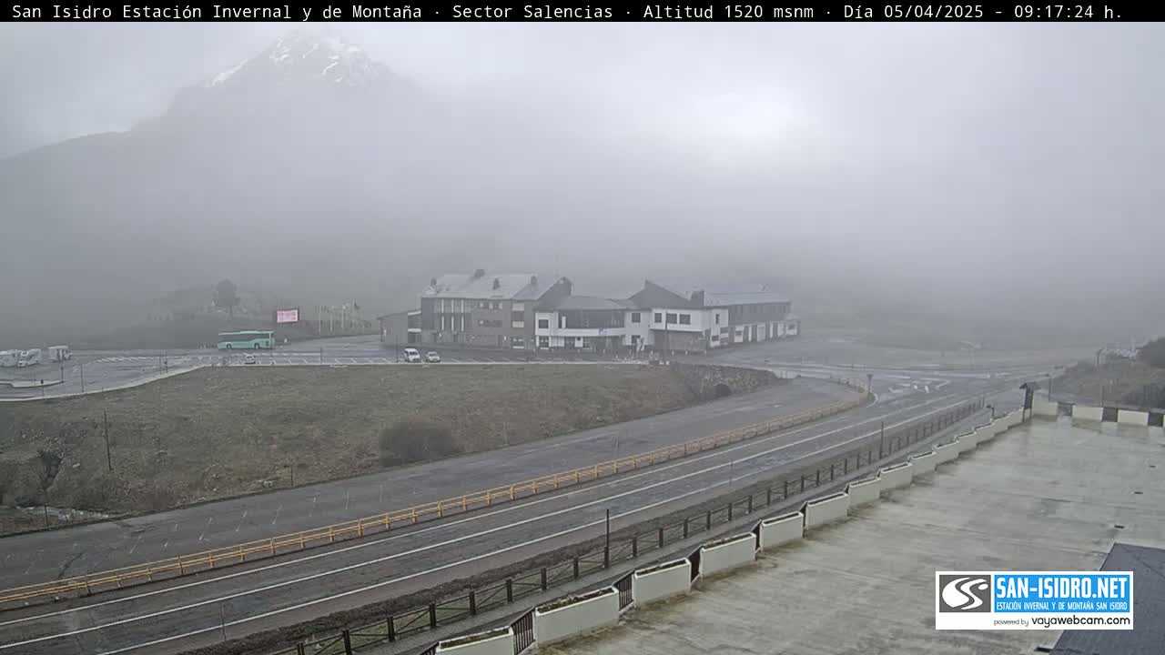 A foggy mountain vista overlooks a parking lot, a roadway, and several buildings.