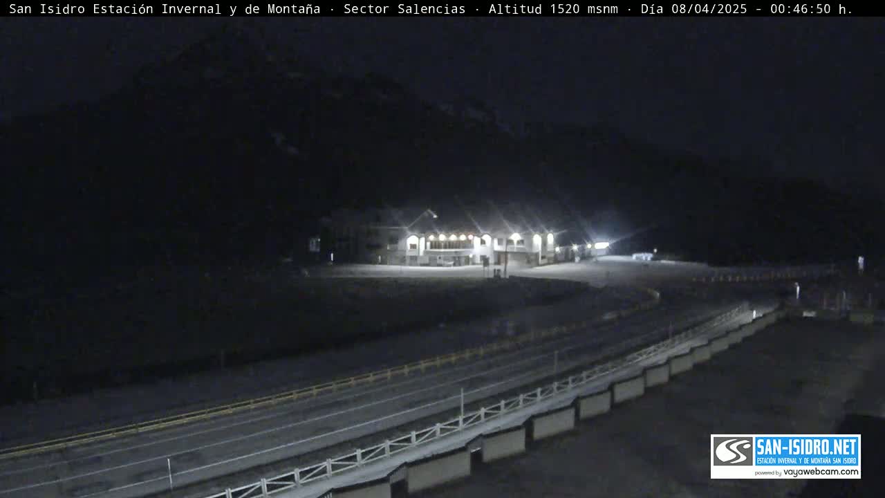 A nighttime view of a snow-covered mountainside with a building and roadway illuminated by artificial lights.