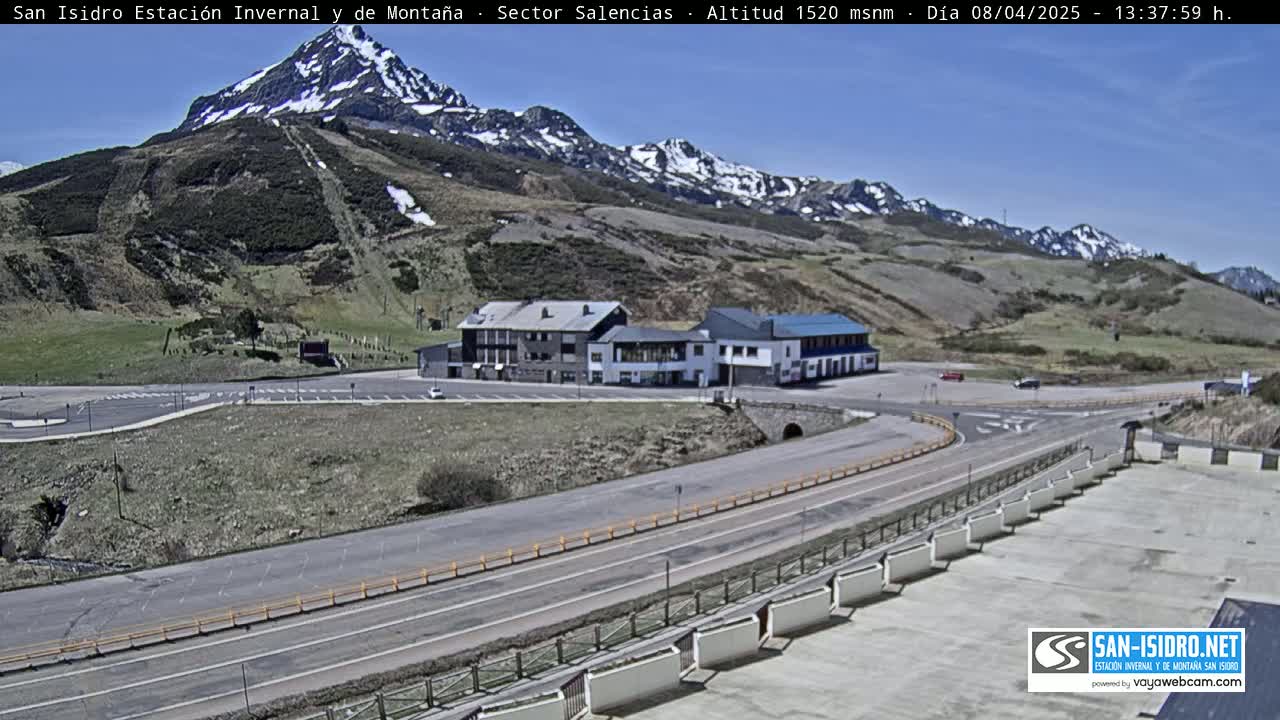 A mountainside resort area with a parking lot, buildings, and roads under a clear, sunny sky.