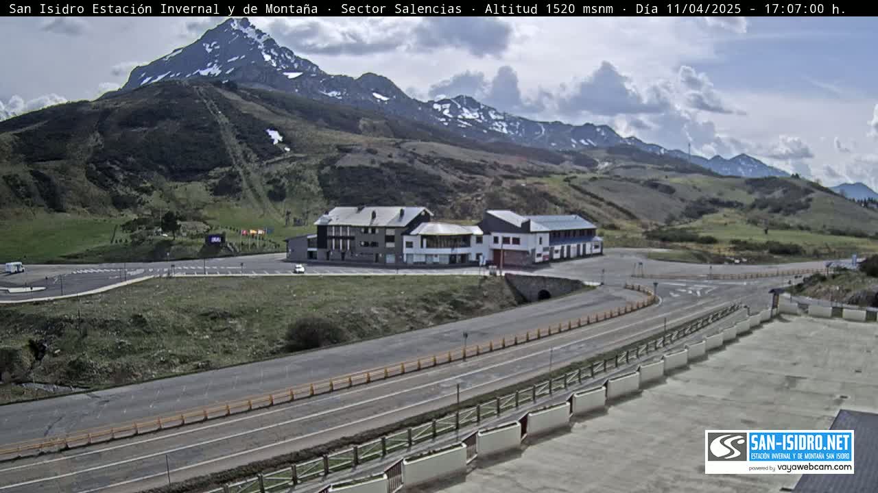 A mountainside parking lot with a large building and a road curving through it, under a partly cloudy sky.