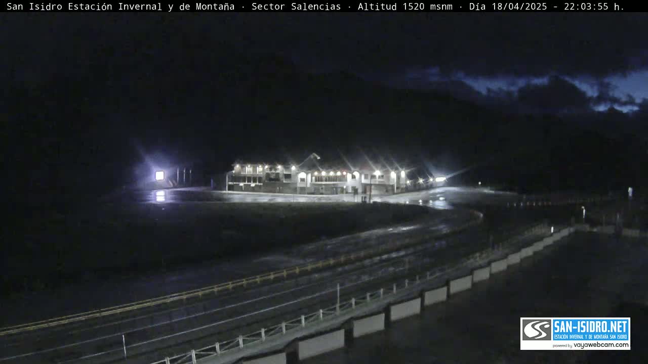 A nighttime view of a building complex, possibly a ski resort, with wet roads and a dark, cloudy sky.