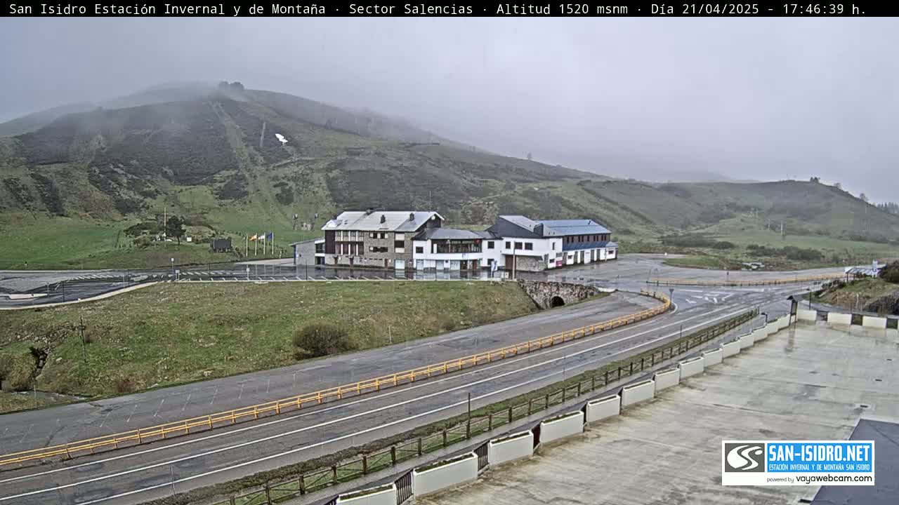 A mountainside with a ski slope, buildings, and a roadway is viewed under overcast conditions.