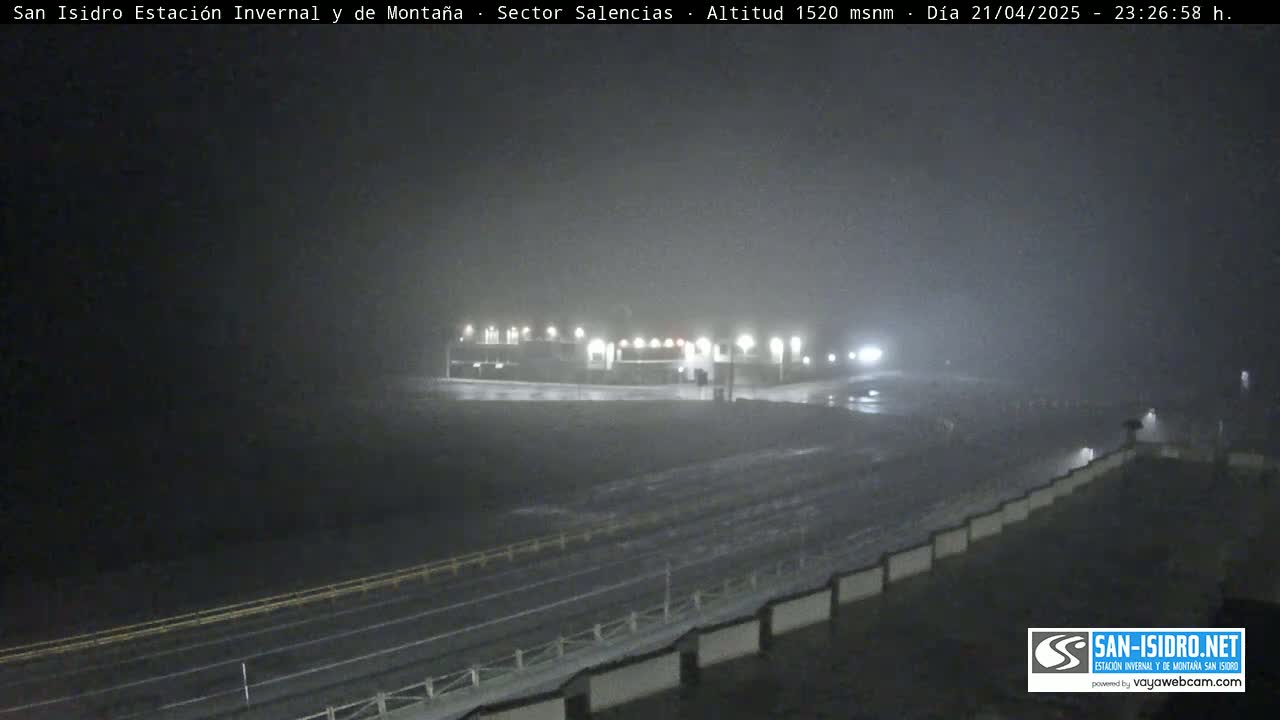 A nighttime view of a snow-covered road leading to a building complex under heavy snow.
