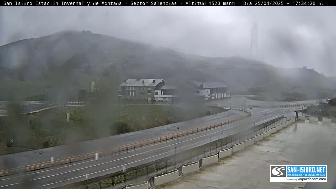 A rainy view of a mountain road and buildings, with a misty mountain in the background.