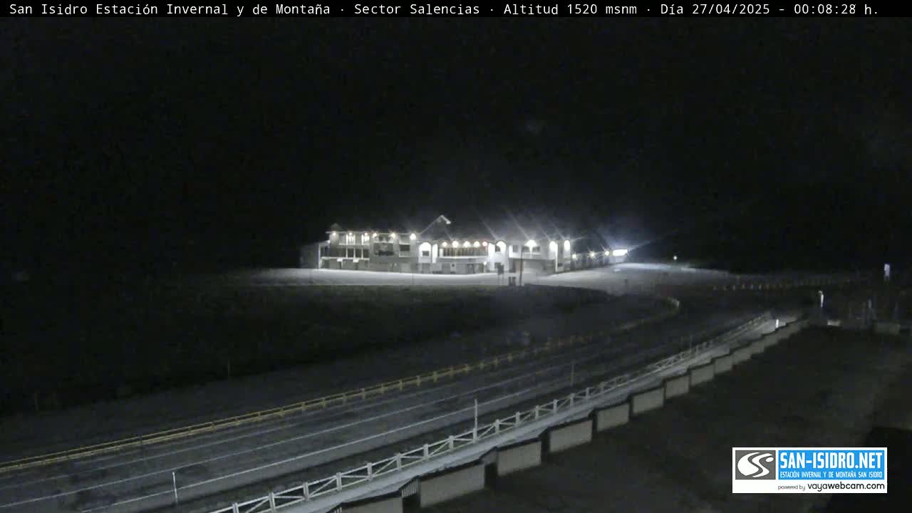 A large building is illuminated at night, overlooking a long, dark road with a low barrier.