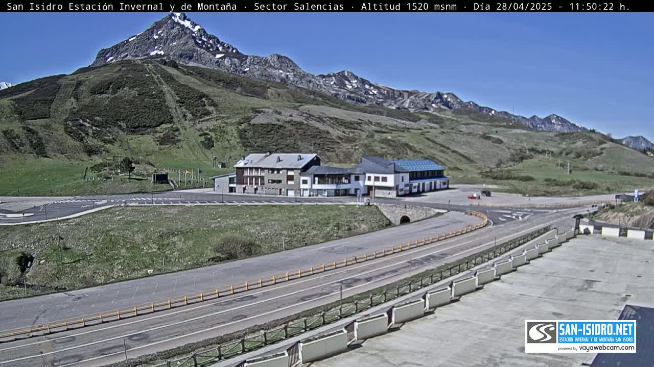 A mountainside resort with a parking lot and roadway is visible under a clear blue sky.