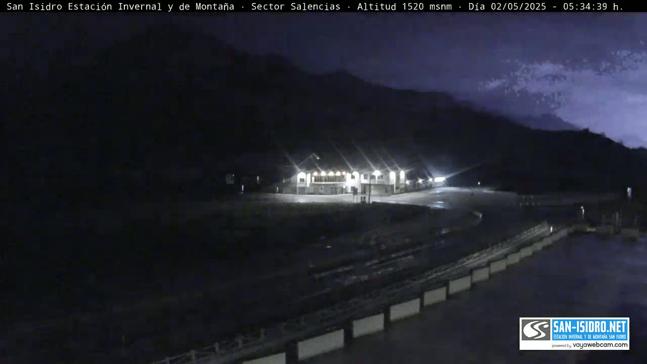 A nighttime view of a building complex illuminated by lights, situated in a mountainous area under a dark, possibly cloudy sky.