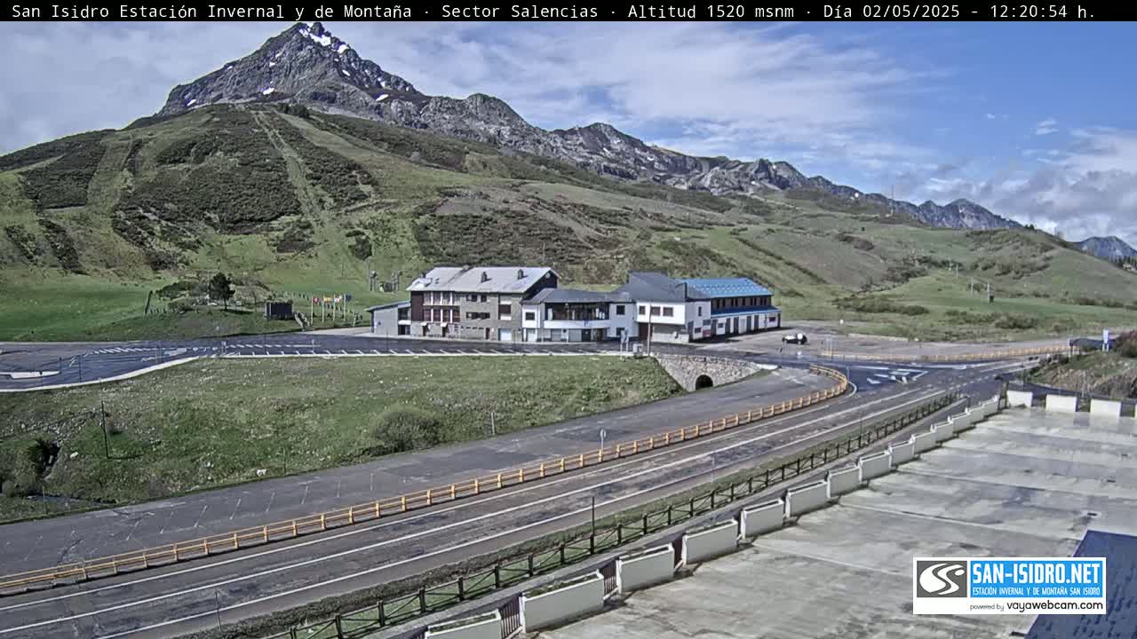 A mountainside resort with buildings and roads sits under a mostly clear blue sky.