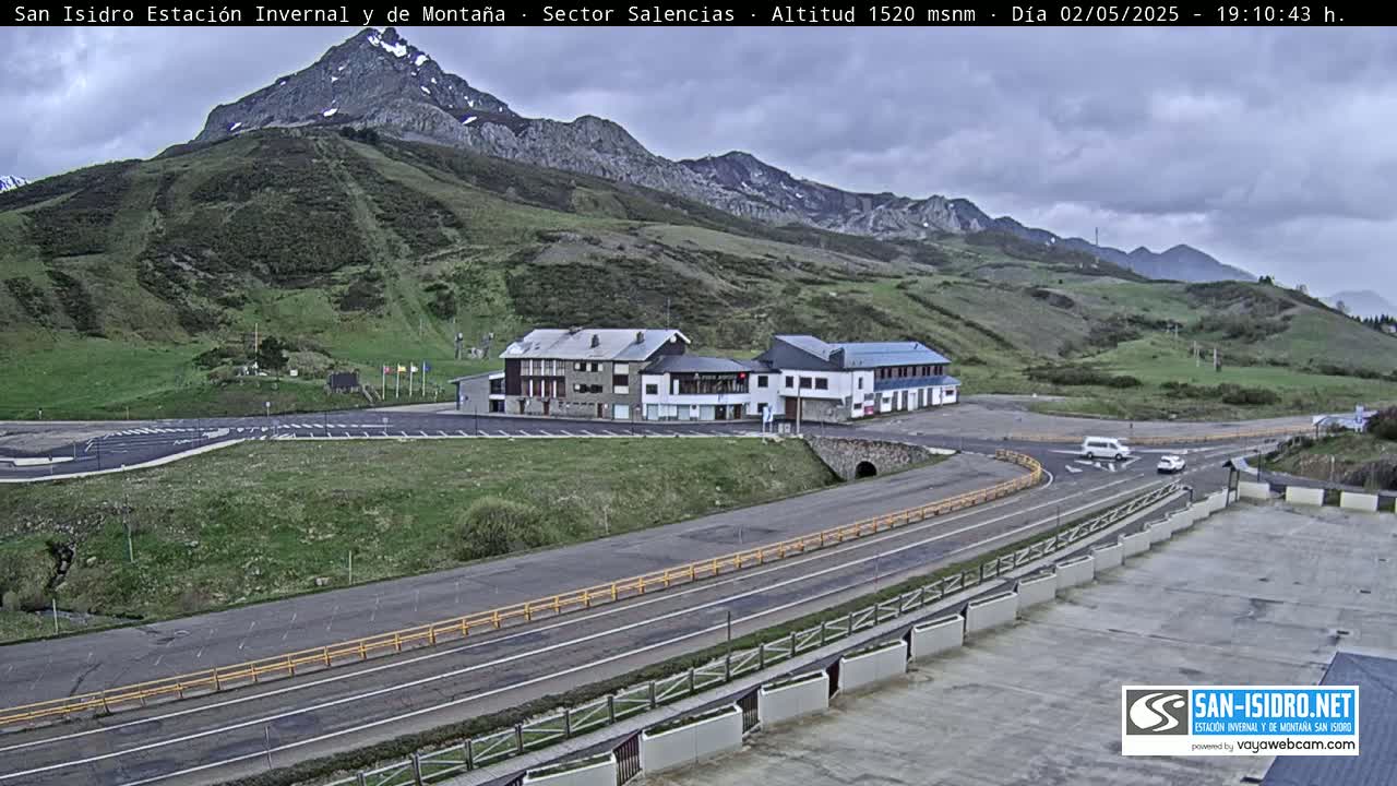 A mountainside parking lot with several buildings and a road curves through it under an overcast sky.