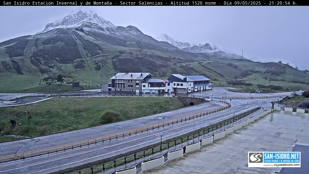 A mountainside ski resort with several buildings near a wet road under an overcast sky.
