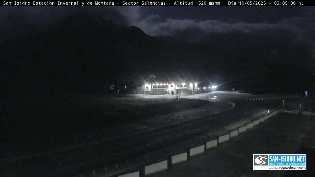 A nighttime, illuminated building sits in a mountain valley under a cloudy sky.