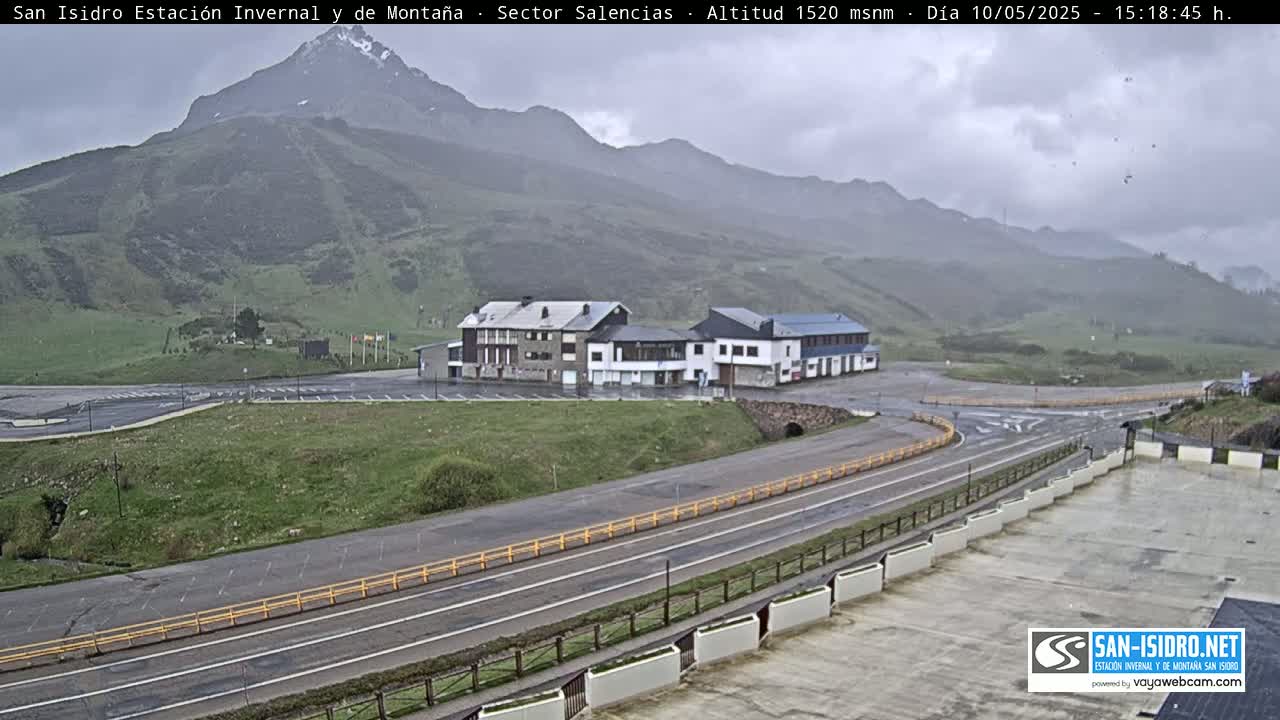 A mountainside view shows a building complex next to a roadway under an overcast sky.