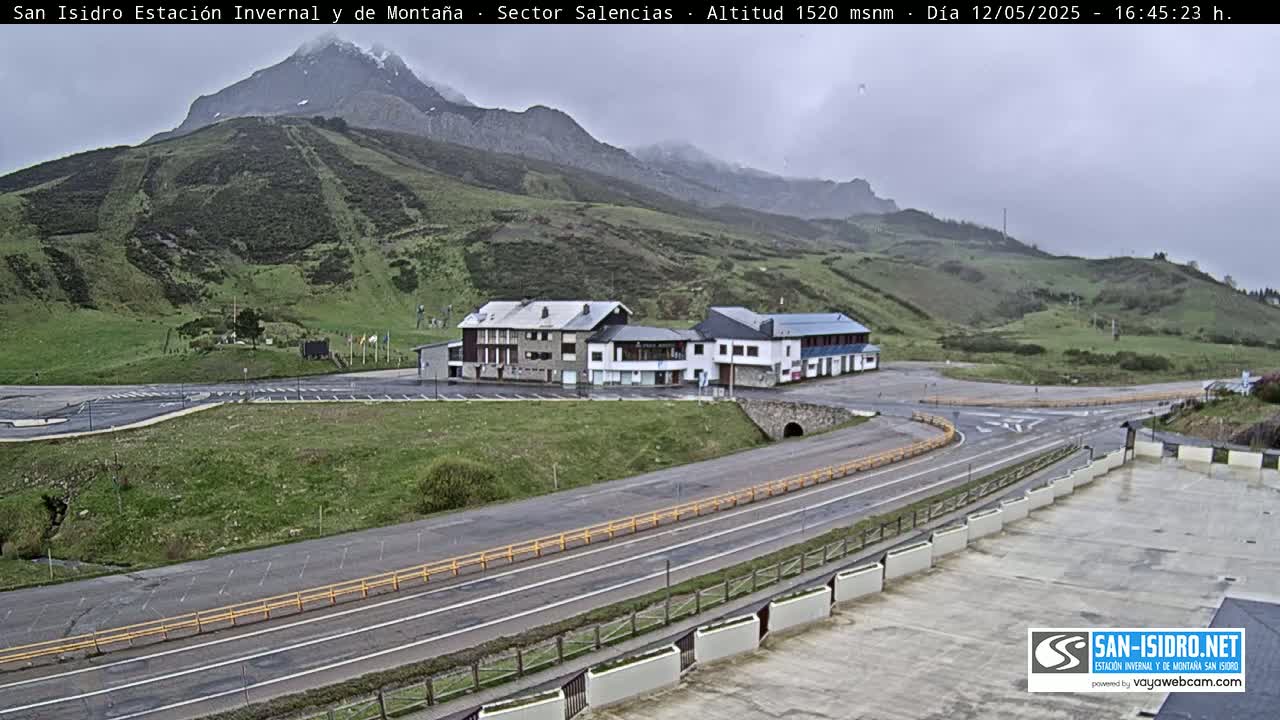 A mountaintop parking lot and roadway overlook a valley under an overcast sky.