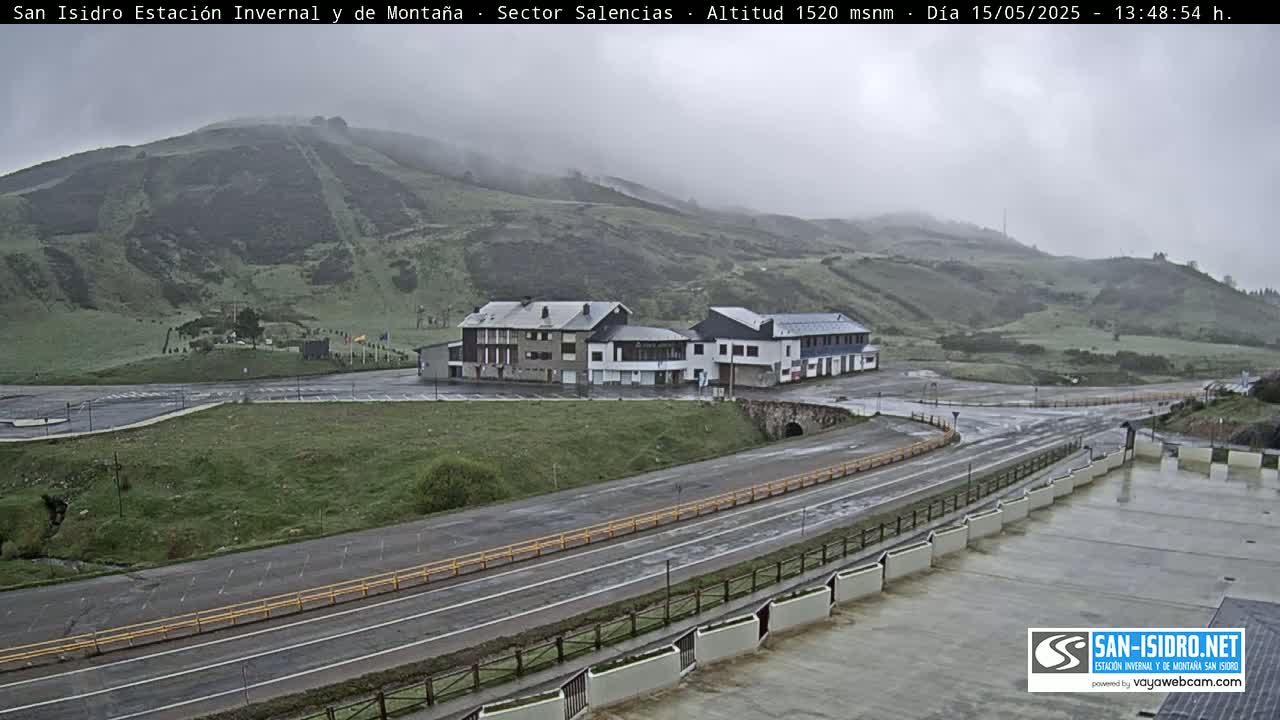 A mountainside with a building complex and roads is visible under an overcast sky.