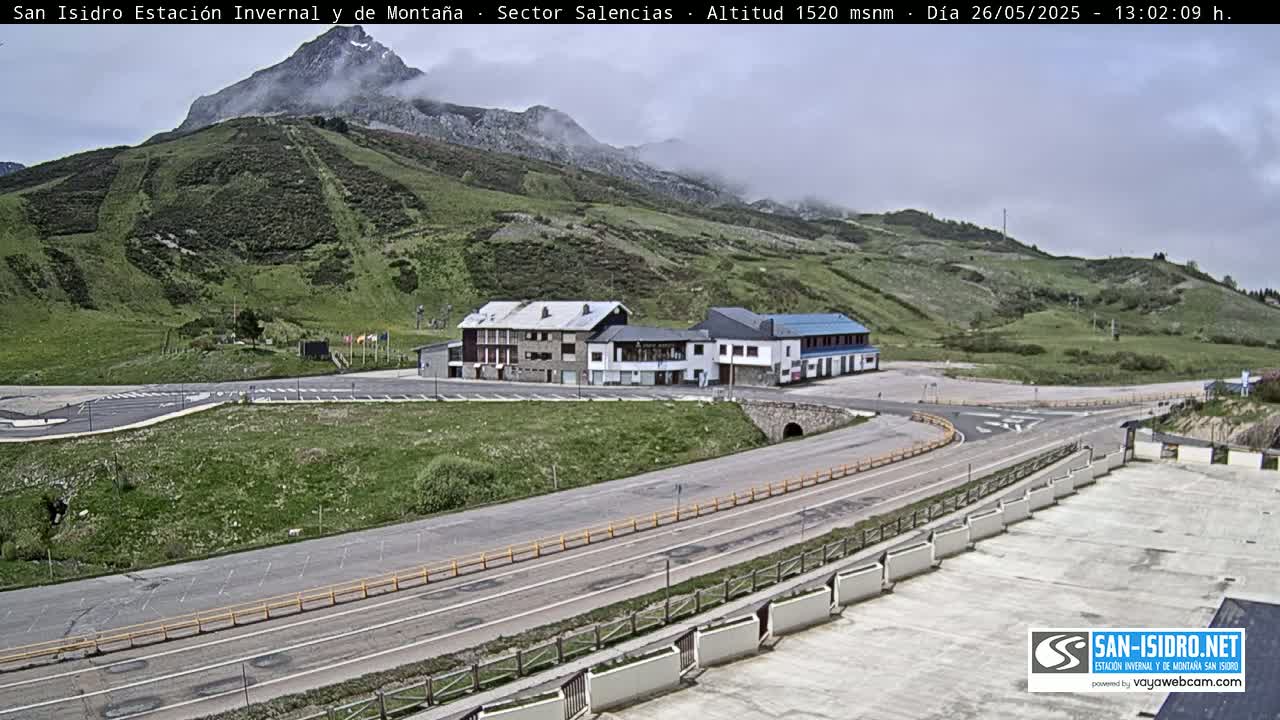 A mountain resort with buildings and roads sits below a partly cloudy mountainside.