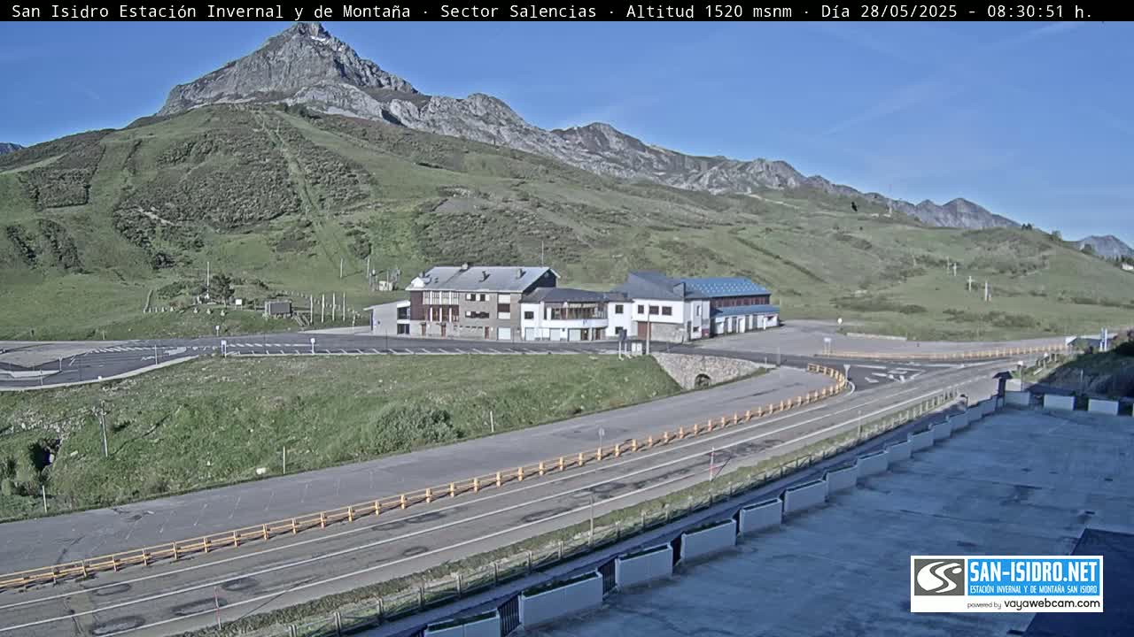 A mountainside parking lot and roadway near a cluster of buildings under a clear blue sky.