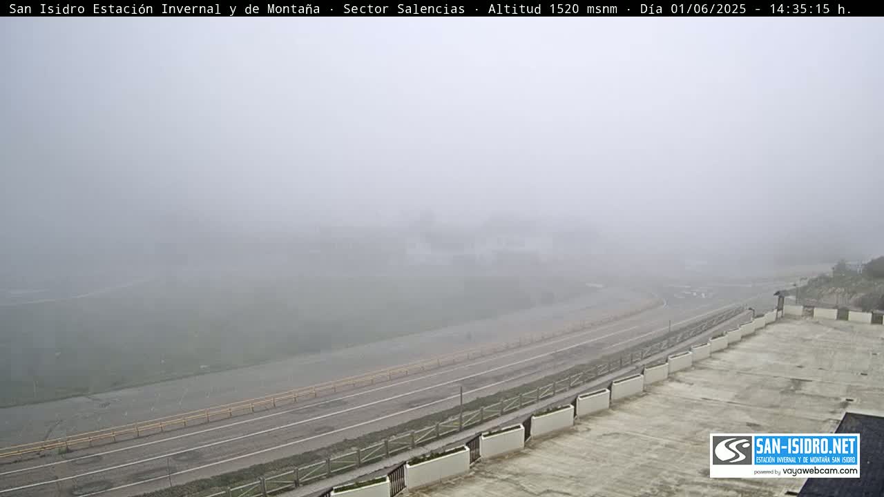 A foggy, high-altitude view of a roadway curving alongside a building with planters, all shrouded in thick mist.